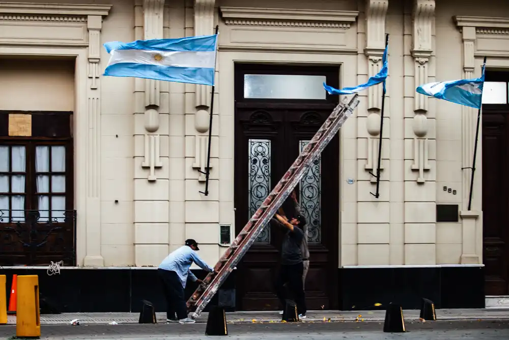 Mientras la movilizaci&oacute;n se desarrollaba a pocos metros, dos trabajadores continuaban sus tareas frente a un edificio p&uacute;blico. La escena registra la convivencia entre el reclamo ciudadano y la rutina cotidiana del centro correntino.
