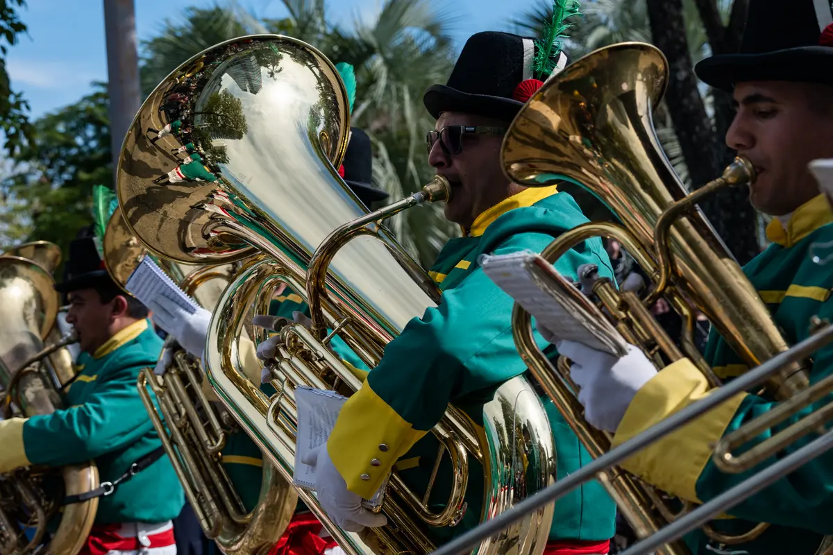 Los instrumentos de viento de las bandas acompa&ntilde;aron el avance de las formaciones y marcaron el pulso de la jornada. Las melod&iacute;as se mezclaron con los aplausos, las conversaciones del p&uacute;blico y el tr&aacute;nsito interrumpido por el paso del desfile.
