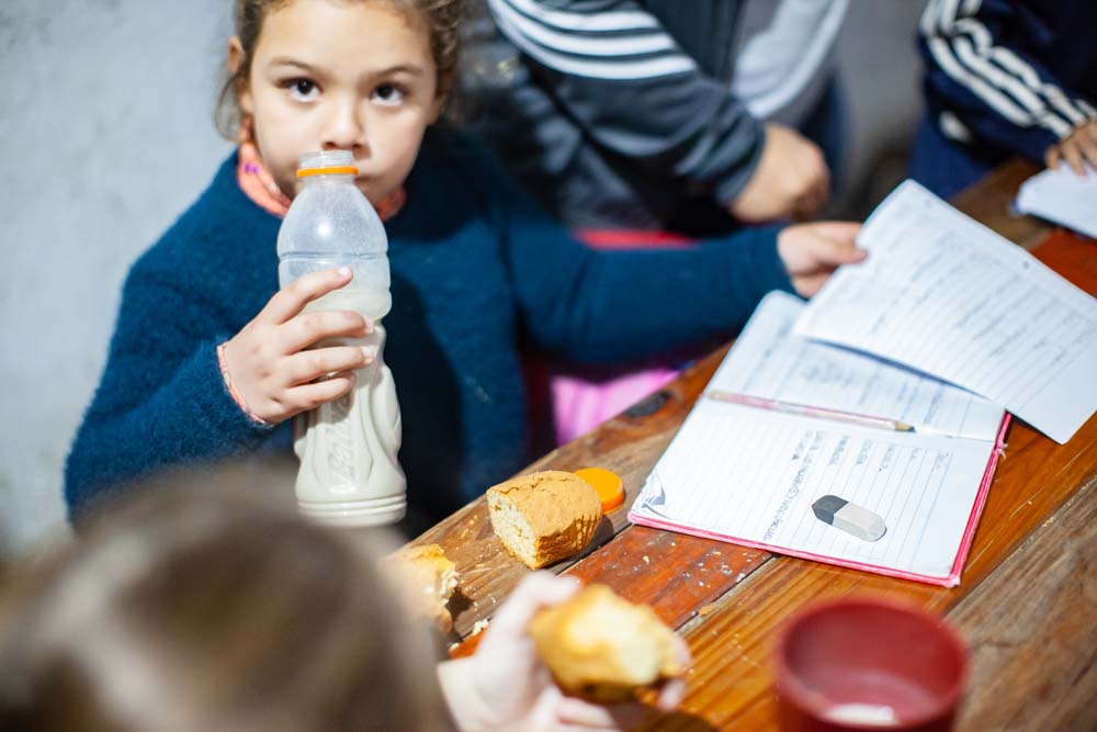 Hacer la tarea con el apoyo de docentes, mientras la merienda se mezcla con cuadernos y lápices, es una constante en un salón repleto de niños.